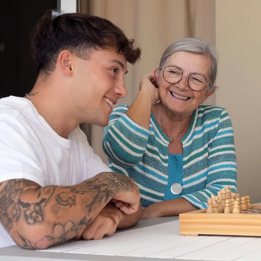 Ein junger Mann und eine ältere Frau lachen gemeinsam an einem Schachbrett